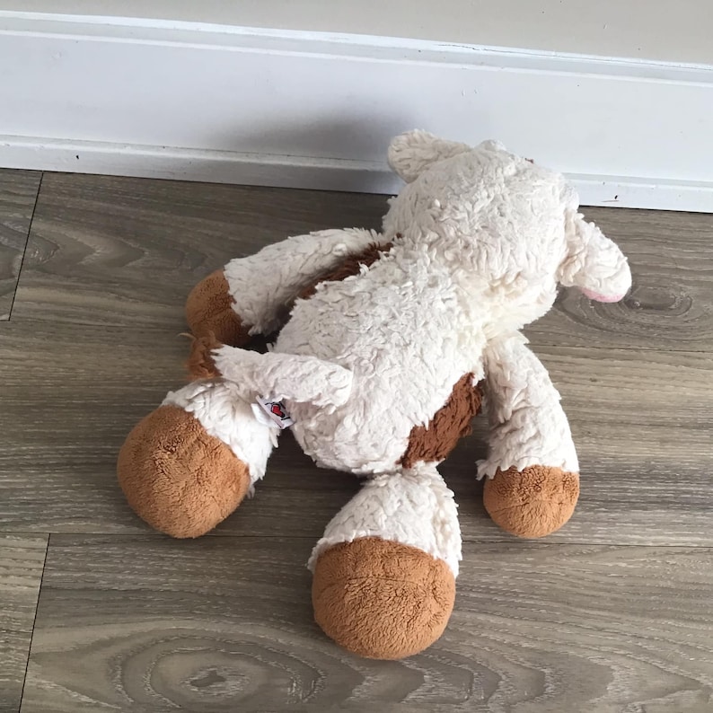 Pu&ograve; includere: Un giocattolo di peluche di mucca bianco e marrone con il naso rosa. Il giocattolo &egrave; sdraiato sulla schiena con le gambe in aria.