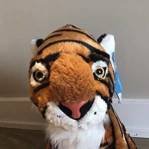 May include: A plush tiger toy with orange and black stripes, white fur around the face, and black eyes with yellow pupils.