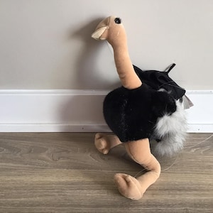 May include: A plush toy ostrich with a black and white body, brown legs, and a long brown neck. The ostrich is lying on its side with its head turned to the side.