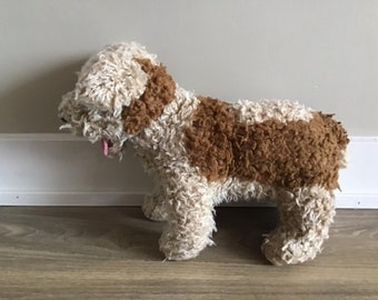 以下が含まれることがあります： カールした質感のデザインが特徴の、犬のぬいぐるみ。クリーム色と茶色の組み合わせで、背中と耳に茶色の部分があります。犬の舌が見えており、四足で立っています。