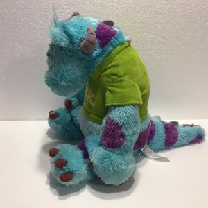 Op de afbeelding: Een blauw en paars pluche speelgoed van het personage Sulley uit de film Monsters Inc. Het speelgoed draagt een groen shirt met het woord "Mike" erop.
