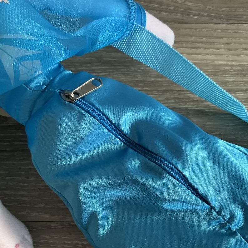 May include: A close-up of a light blue satiny bag with a zipper closure and a blue strap. The bag has a silver zipper and a white interior. The bag is likely a children's accessory.