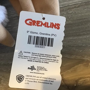 May include: A plush Gizmo doll from the Gremlins movie, with a tag that reads "9" Gizmo, Gremlins (PV)". The tag also includes a barcode and safety information. The doll is tan with white fur.