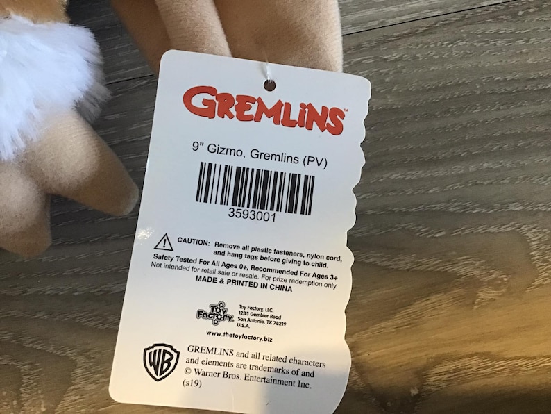 May include: A plush Gizmo doll from the Gremlins movie, with a tag that reads "9" Gizmo, Gremlins (PV)". The tag also includes a barcode and safety information. The doll is tan with white fur.