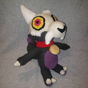 May include: A crocheted plush toy of King from the Owl House. The toy is black, purple, and white with a yellow and red eye.