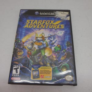 May include: A Nintendo GameCube video game case for Starfox Adventures featuring a blue background with a group of anthropomorphic animal characters. The cover includes the title in yellow text, an ESRB Teen rating, and a bonus offer sticker.