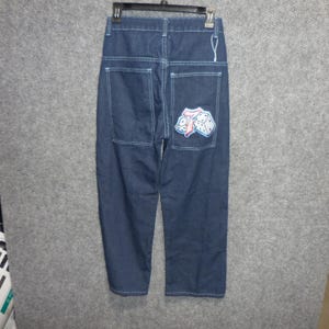 May include: Dark blue denim jeans featuring a high-waisted design with white contrast stitching. The back of the jeans includes two large patch pockets, with a graphic patch of two dice and the number seven embroidered on the right pocket.