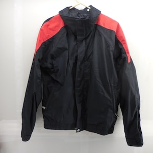 May include: A black jacket with red panels on the shoulders and upper sleeves. The jacket features a high collar, a front zipper closure, and long sleeves with adjustable cuffs. The design includes side pockets with zippers and a straight hemline.
