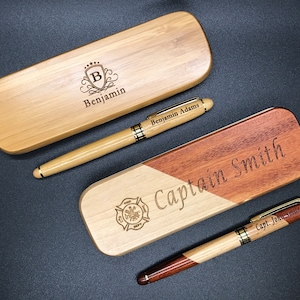 May include: Two wooden pen boxes with engraved names and a pen in each. The box on the left is light brown with the name "Benjamin" engraved on it. The box on the right is a two-toned wood with the name "Captain Smith" engraved on it. The pen in the left box is engraved with "Benjamin Adams". The pen in the right box is engraved with "Capt. John Smith".