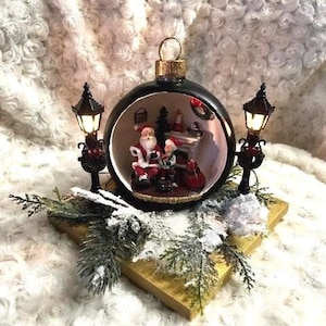 Christmas Ornament Diorama with Santa and an Elf in his house by the fire, with battery operated lanterns