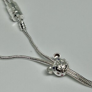 K&ouml;nnte beinhalten: Ein silbernes Kettenarmband mit einem silbernen Anh&auml;nger in Form eines Comic-Mauskopfes mit blauen und roten Edelsteinen.