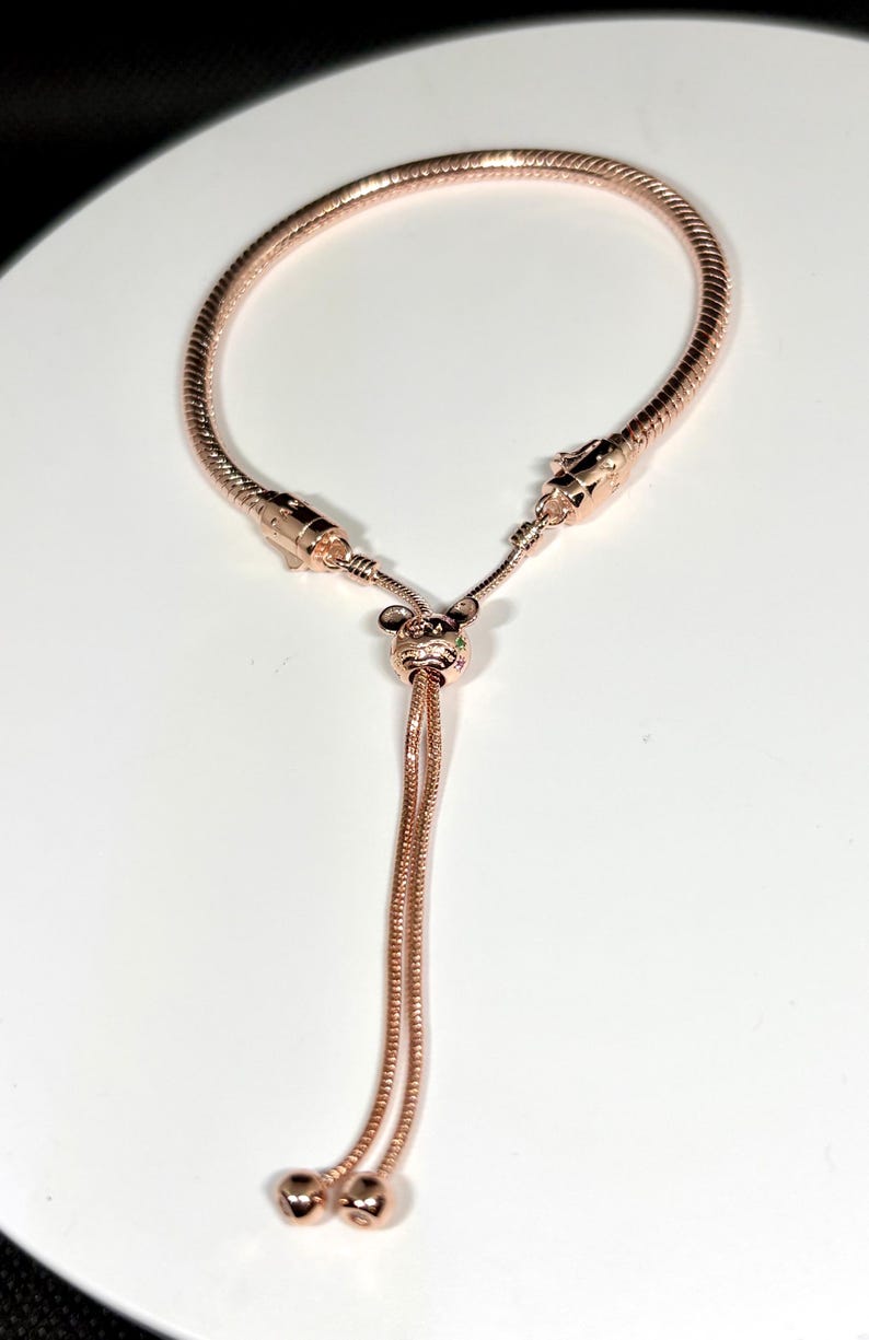 Op de afbeelding: Verstelbare armband in ros&eacute;goud met een slangenkettingontwerp. De armband heeft een Mickey Mouse-vormige bedel met kleine, kleurrijke edelstenen. De uiteinden van de armband hebben twee kleine, ronde kralen.