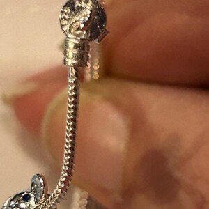 K&ouml;nnte beinhalten: Ein silbernes Armband mit einem silbernen Anh&auml;nger in Form eines kleinen Elefanten. Der Anh&auml;nger hat einen blauen Stein an seinem R&uuml;ssel.