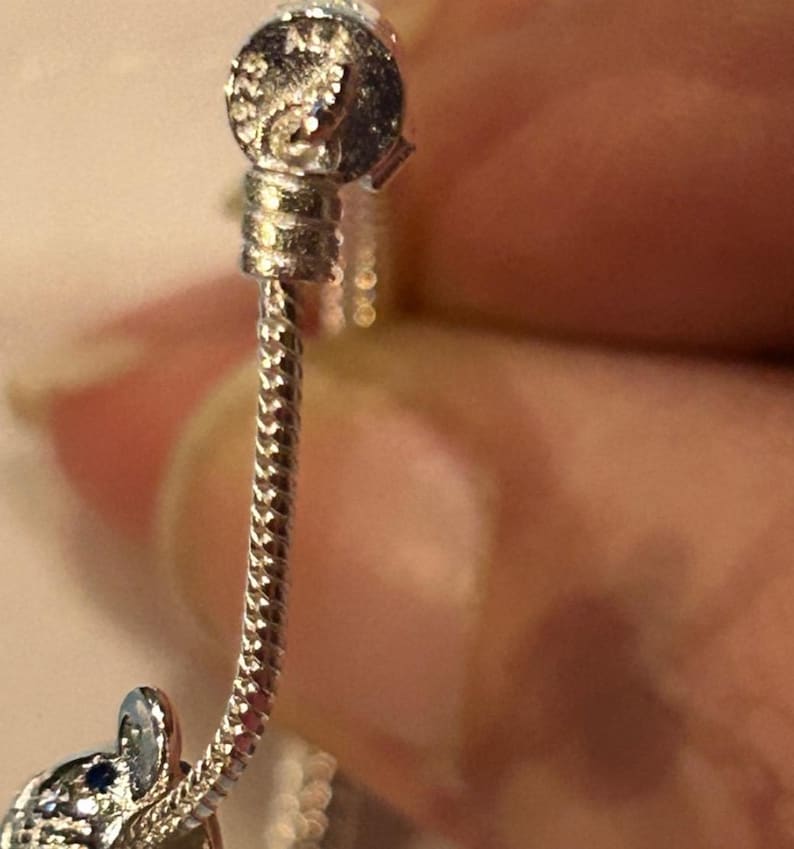 K&ouml;nnte beinhalten: Ein silbernes Armband mit einem silbernen Anh&auml;nger in Form eines kleinen Elefanten. Der Anh&auml;nger hat einen blauen Stein an seinem R&uuml;ssel.