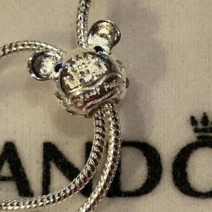 K&ouml;nnte beinhalten: Silbernes Charm-Armband mit einem silbernen Mickey-Maus-Anh&auml;nger mit einem rosa und blauen Stein. Der Anh&auml;nger tr&auml;gt die Worte "Disney Parks" eingraviert.