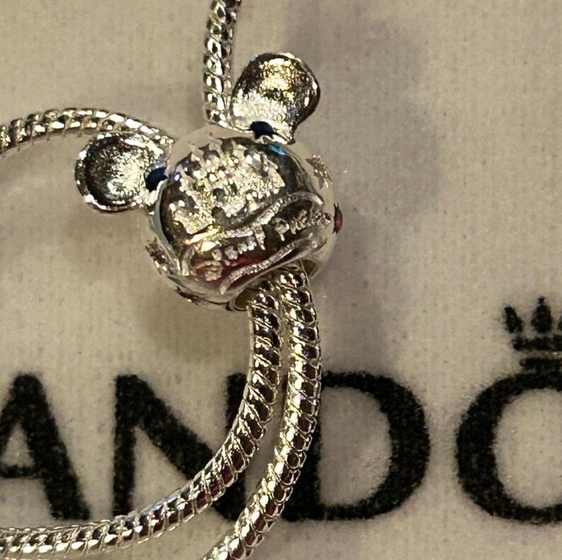 K&ouml;nnte beinhalten: Silbernes Charm-Armband mit einem silbernen Mickey-Maus-Anh&auml;nger mit einem rosa und blauen Stein. Der Anh&auml;nger tr&auml;gt die Worte "Disney Parks" eingraviert.