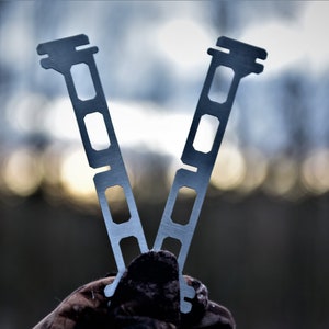 Peut inclure: Deux supports de réchaud de camping en métal argenté avec une série de découpes rectangulaires.