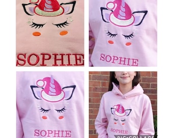 May include: Pink hooded sweatshirt with a unicorn wearing a Santa hat embroidered on the front. The sweatshirt has the name "SOPHIE" embroidered on the bottom.