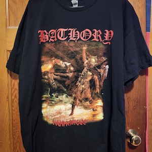 May include: A black short-sleeve t-shirt featuring a graphic print on the front. The text BATHORY is printed in red at the top, and HAMMERHEART is printed in red at the bottom. The central graphic depicts a warrior in a helmet and fur clothing.
