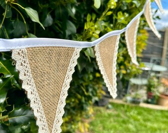 May include: A burlap banner with white lace trim. The banner is strung between two trees and has a rustic, vintage look.