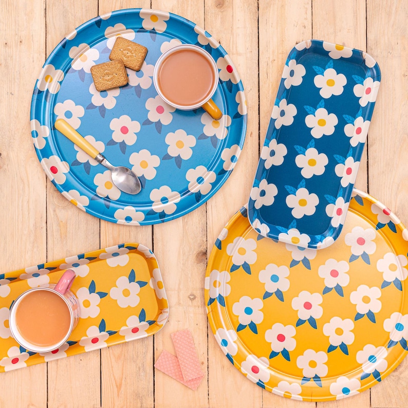 May include: Four round and rectangular trays with a floral pattern. The trays are blue and yellow with white flowers. Two of the trays have a cup of tea on them. One tray has biscuits on it.