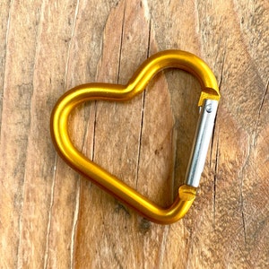 May include: A gold heart-shaped carabiner clip with a silver gate.