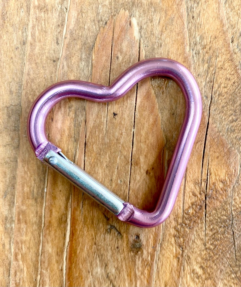 May include: A pink metal heart-shaped carabiner with a silver metal clasp.