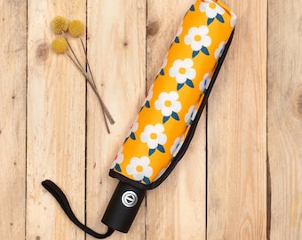 May include: A yellow umbrella with a white floral pattern. The umbrella is closed and has a black handle.