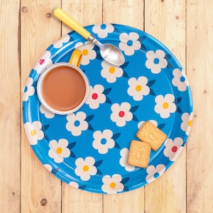 Könnte beinhalten: Ein rundes Tablett mit blauem und weißem Blumenmuster, darauf eine Tasse Tee und zwei Kekse. Das Tablett hat einen gelben Rand.