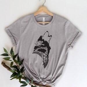 May include: A heather grey t-shirt with a black silhouette of a wolf howling, with trees and leaves forming the wolf's body.