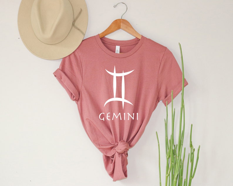 May include: A dusty rose t-shirt with a white Gemini zodiac symbol and the word "GEMINI" printed on the front.