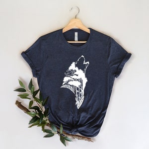May include: A dark blue t-shirt with a white graphic of a wolf howling with trees growing out of its silhouette.