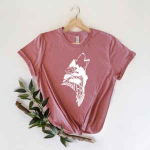 May include: A mauve t-shirt with a white graphic of a wolf howling with trees growing out of its head.