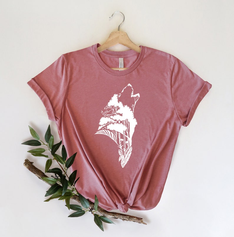 May include: A mauve t-shirt with a white graphic of a wolf howling with trees growing out of its head.