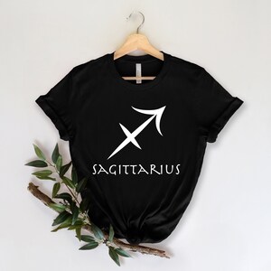 May include: Black t-shirt with a white Sagittarius zodiac symbol and the word "SAGITTARIUS" printed on the front.