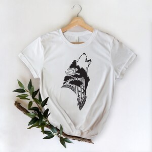 May include: White t-shirt with a black silhouette of a wolf howling, with trees and foliage forming the wolf's body.