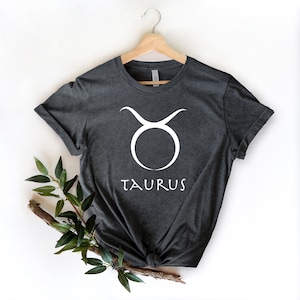 May include: A dark gray t-shirt with a white Taurus zodiac symbol and the word "TAURUS" printed on the front.