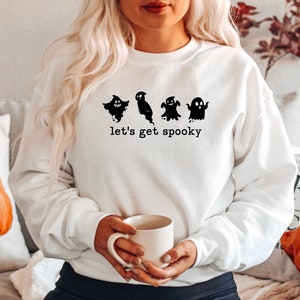 May include: White sweatshirt with a black graphic of four ghosts and the text "let's get spooky".