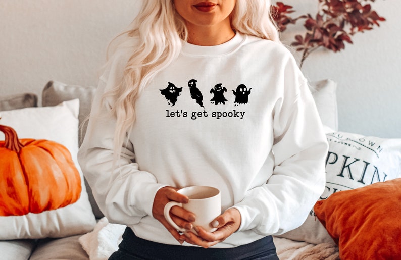 May include: White sweatshirt with a black graphic of four ghosts and the text "let's get spooky".
