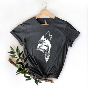 May include: A dark gray t-shirt with a white graphic of a wolf howling with trees growing out of its head.