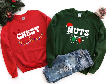 Puede incluir: Dos sudaderas con temática navideña, una roja con el texto "CHEST" y la otra verde con el texto "NUTS". Ambas sudaderas tienen una cadena de luces navideñas con un gorro de Papá Noel en la sudadera verde.
