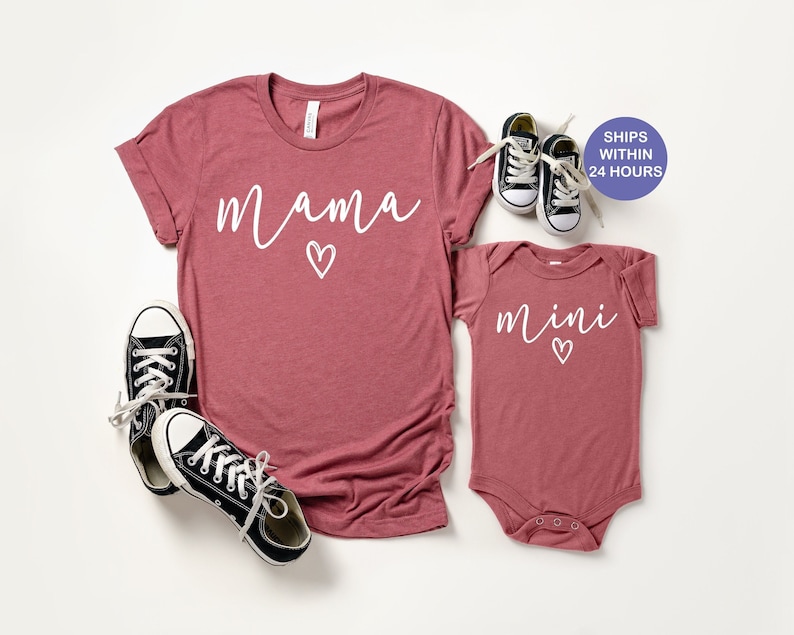 May include: A set of two shirts in a dusty rose color. The larger shirt has the word "mama" written in white with a small heart. The smaller shirt has the word "mini" written in white with a small heart.