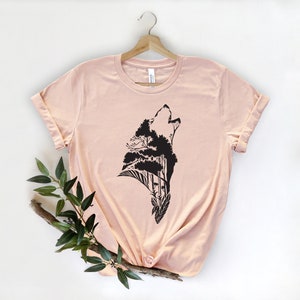 May include: A light pink t-shirt with a black silhouette of a wolf howling with trees growing out of its head.