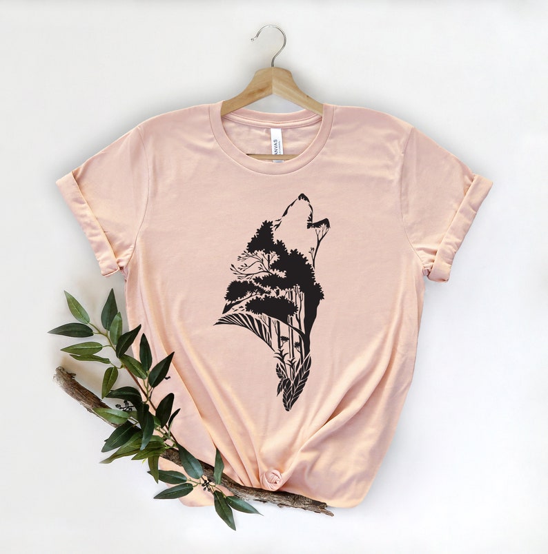 May include: A light pink t-shirt with a black silhouette of a wolf howling with trees growing out of its head.