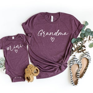 May include: A set of two maroon t-shirts with white text. The larger shirt says "Grandma" with a small heart. The smaller shirt says "mini" with a small heart.