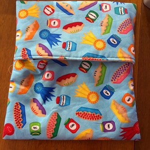 May include: A blue fabric pouch with a colorful pattern of pies, ribbons, and jars of jam. The fabric has a white background with a blue border.