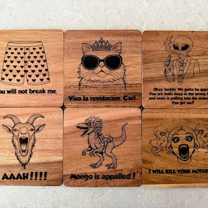 May include: A set of six square wooden coasters featuring laser-engraved illustrations and text. Designs include heart-patterned boxers, a cat with sunglasses and a crown, an alien, a screaming goat, a dinosaur, and a face with pigtails.