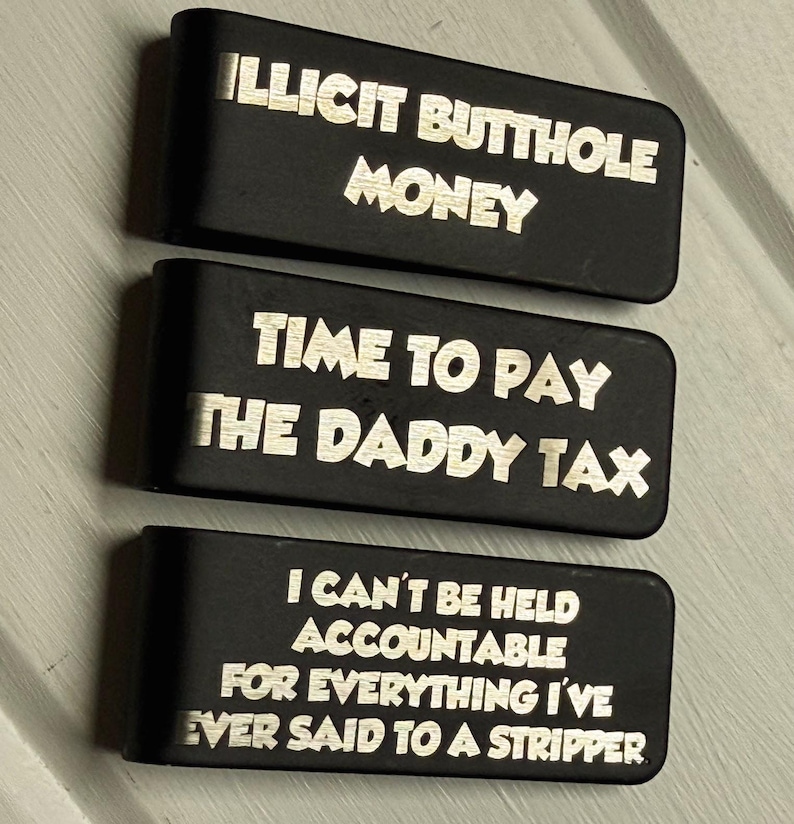 May include: Three rectangular black metal money clips featuring laser-engraved text. The top clip reads ILLICIT BUTTHOLE MONEY, the middle clip reads TIME TO PAY THE DADDY TAX, and the bottom clip reads I CAN'T BE HELD ACCOUNTABLE FOR EVERYTHING I'VE EVER SAID TO A STRIPPER.