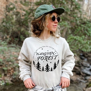 May include: A light gray sweatshirt with a black graphic print of a circle with trees and stars. The text inside the circle reads "Fangorn Forest. Home of the oldest living thing that still walks beneath the sun."