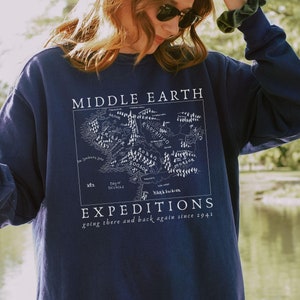 Pode incluir: Uma camisa de moletom azul marinho com um gráfico branco de um mapa da Terra-média, com o texto "Middle Earth Expeditions going there and back again since 2941".